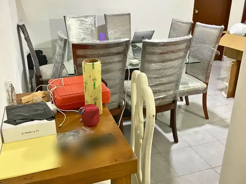 Comedor antes de la limpieza, con sillas envueltas y objetos sobre la mesa, en Guadalupe Tepeyac