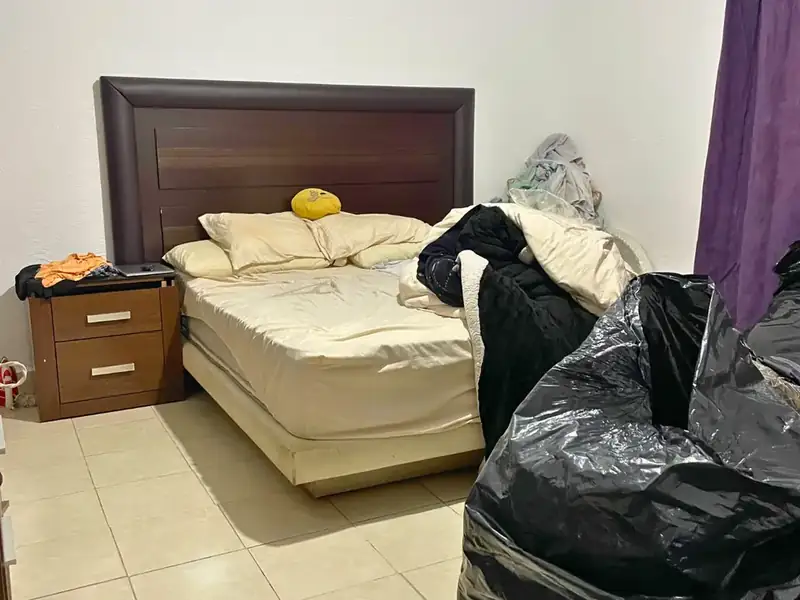 Recámara antes de la limpieza, con ropa sobre la cama y bolsas en el piso, en Guadalupe Tepeyac