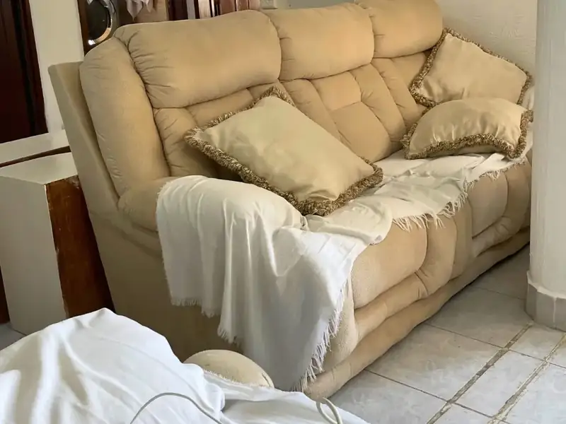 Sala antes de la limpieza, con sábanas y cojines desordenados sobre el sillón, en Guadalupe Tepeyac
